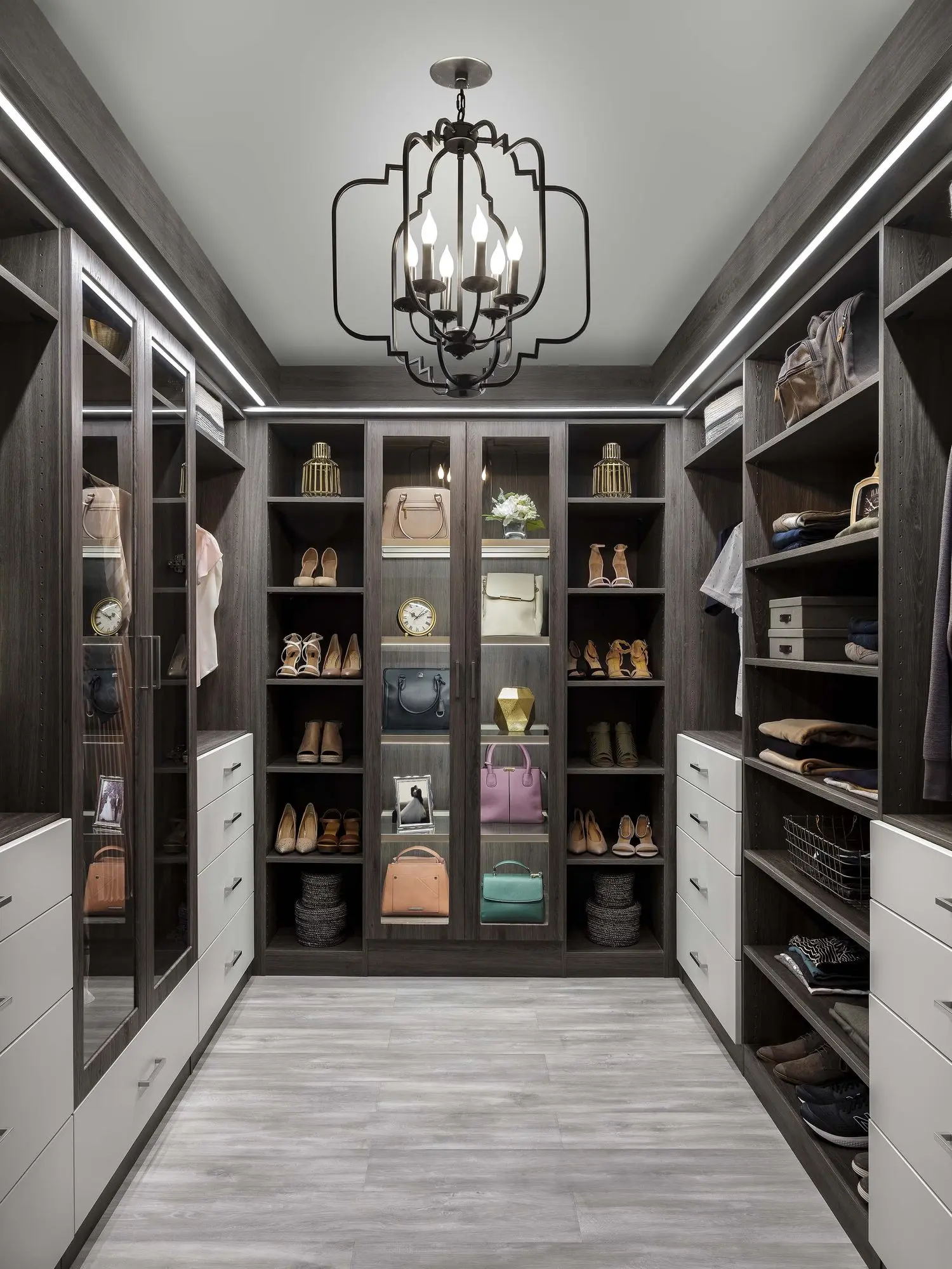 Walk-in closet in Ash with glass-front towers, lit shelving and a chandelier